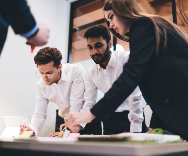 From below of group of multiracial colleagues standing around table and writing notes on stickers while preparing business plan during cowork in office